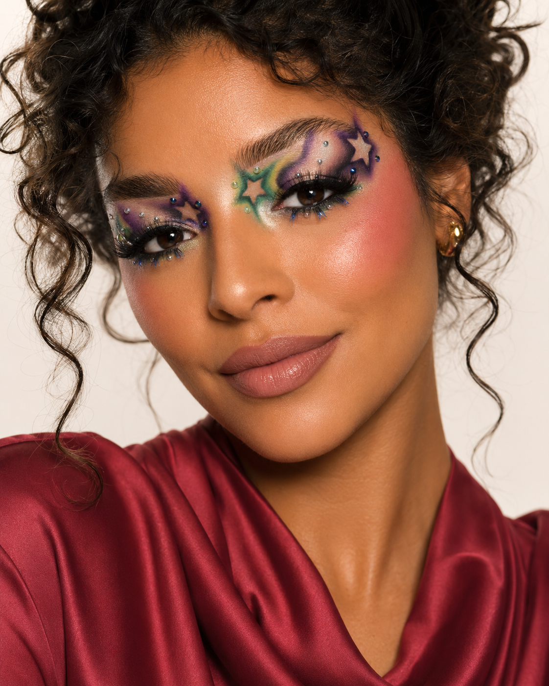 Woman with colorful eye makeup wearing a red top against a neutral background. Part of the Soy Nous campaign.